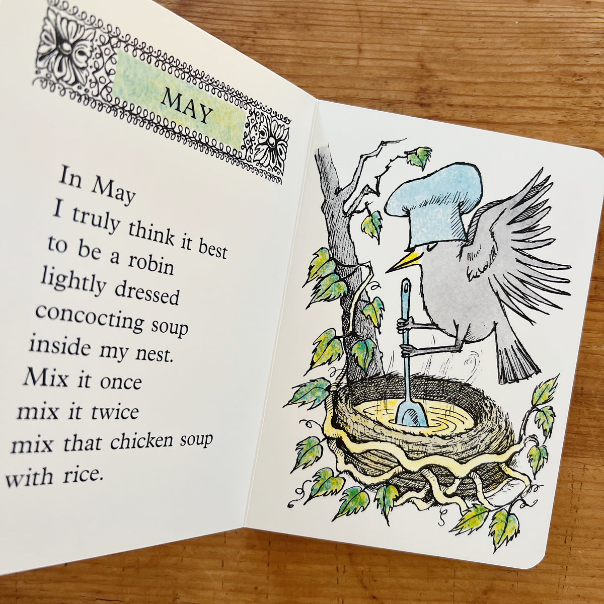 Open interior spread of Chicken Soup with Rice showing the May page: on the left, the verse "In May I truly think it best to be a robin lightly dressed concocting soup inside my nest. Mix it once mix it twice mix that chicken soup with rice."; on the right, a color illustration of a robin in a chef's hat stirring soup in a nest among tree branches and leaves, displayed on a warm wood surface.