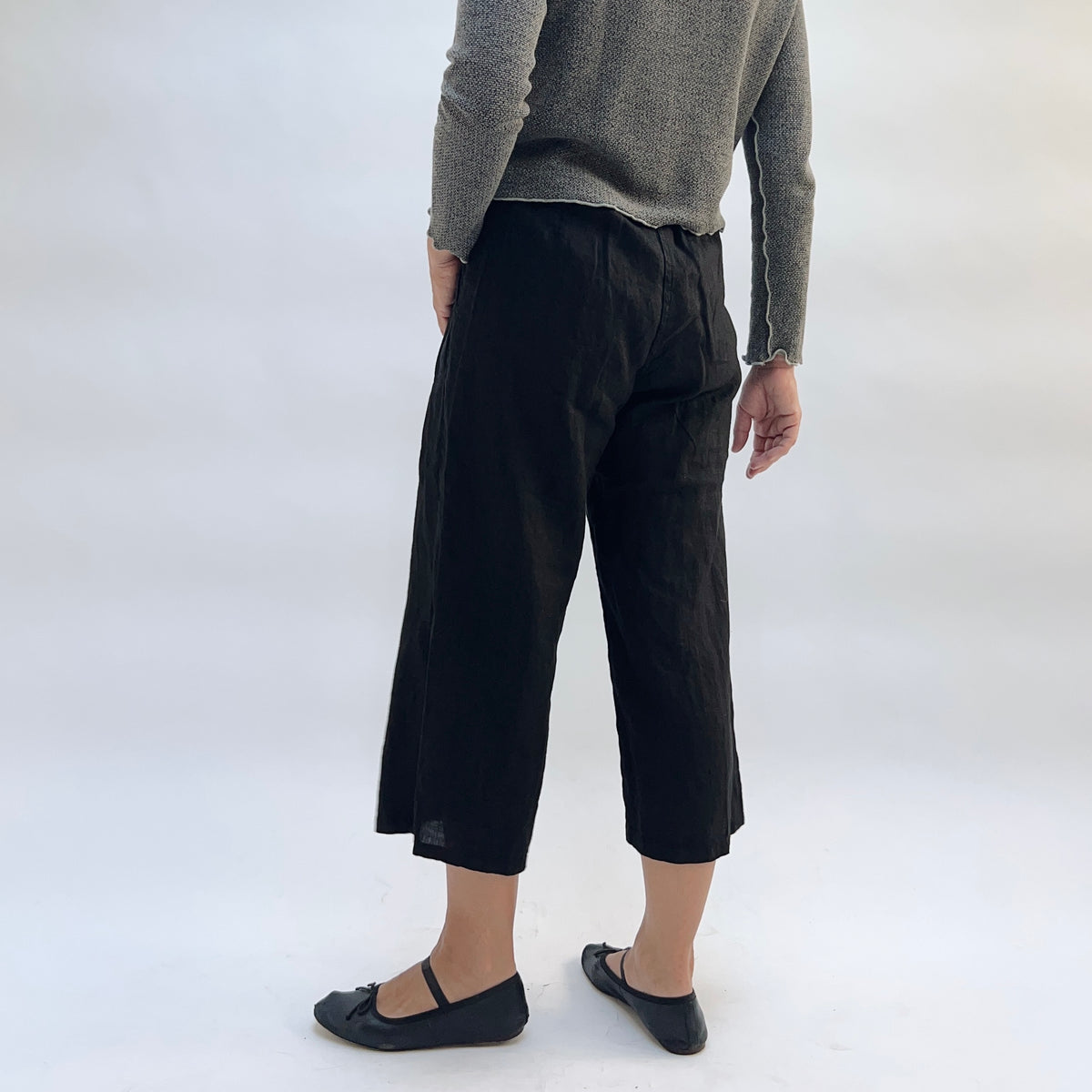 Cut Loose Hanky Linen Easy Crop Flood Pant in Black, black linen wide-leg crop pant, styled with a grey button-front cardigan and black Mary Jane flats — back view showing elastic waistband, wide leg, and straight hem