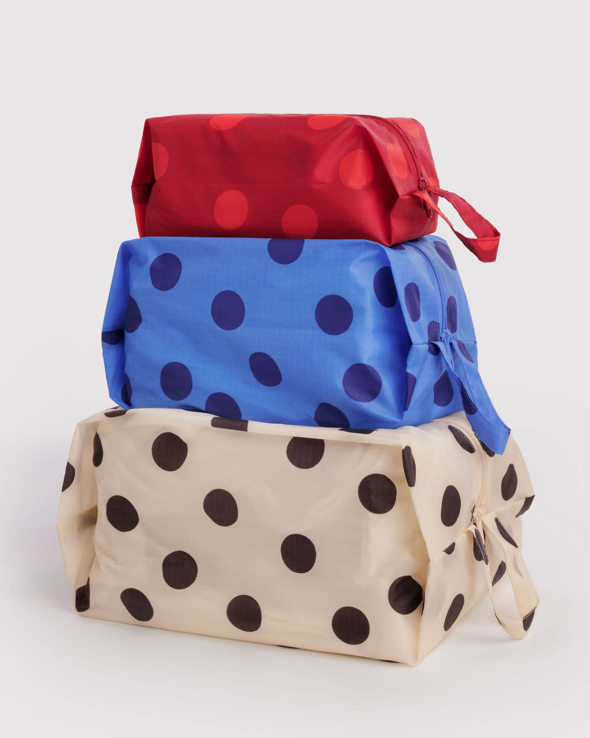 BAGGU 3D Zip Set in Polka Dot Mix, three zippered pouches stacked in red, blue, and cream polka dot patterns, with carrying loops.