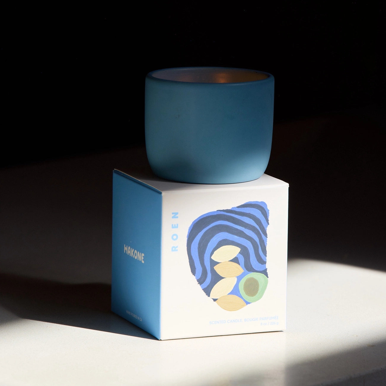 Blue candle on a white box with a blue label against a dark background