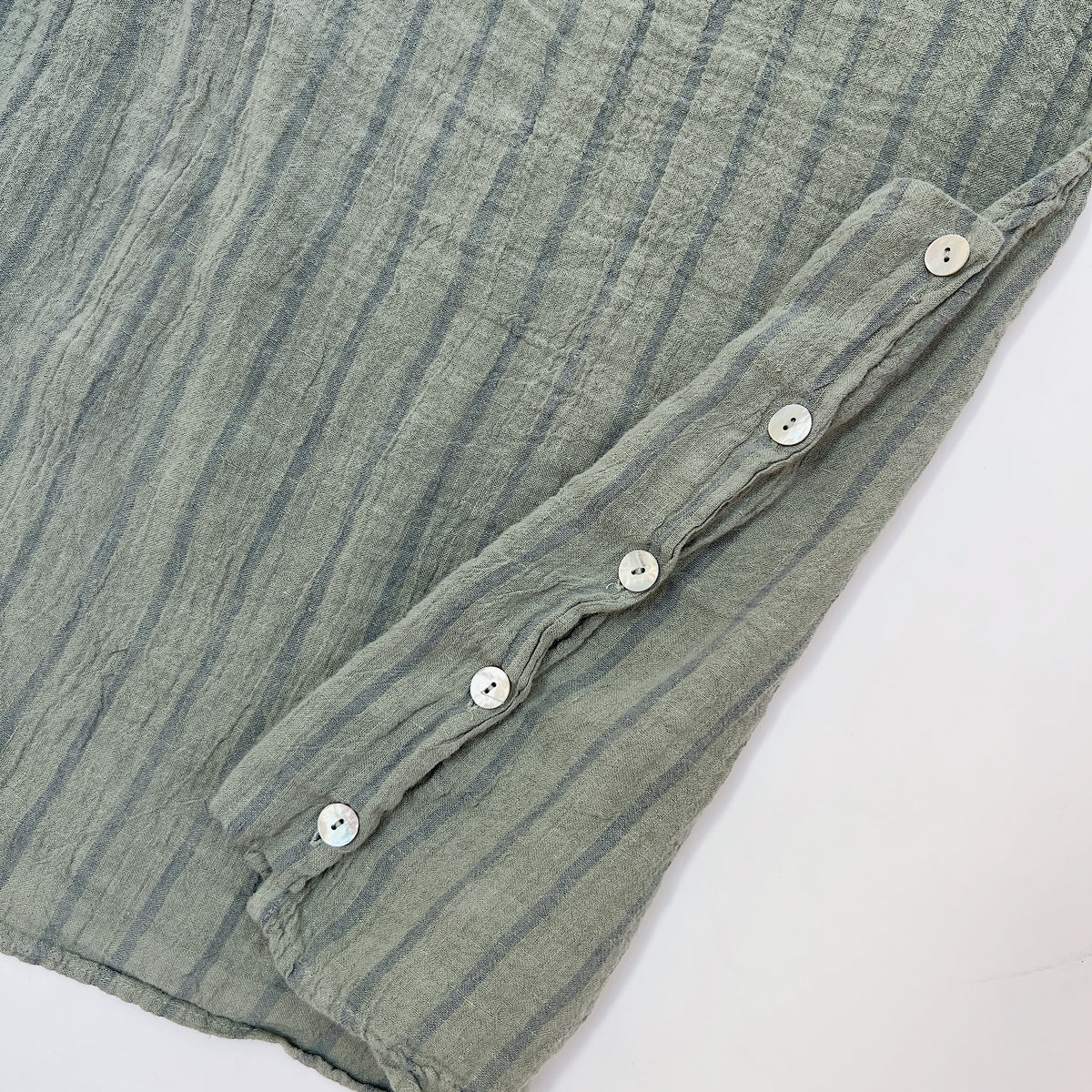 Close-up detail of five white buttons along the side seam of the Cut Loose Striped Side Button Shell Tank in Balsam Green, 100% linen