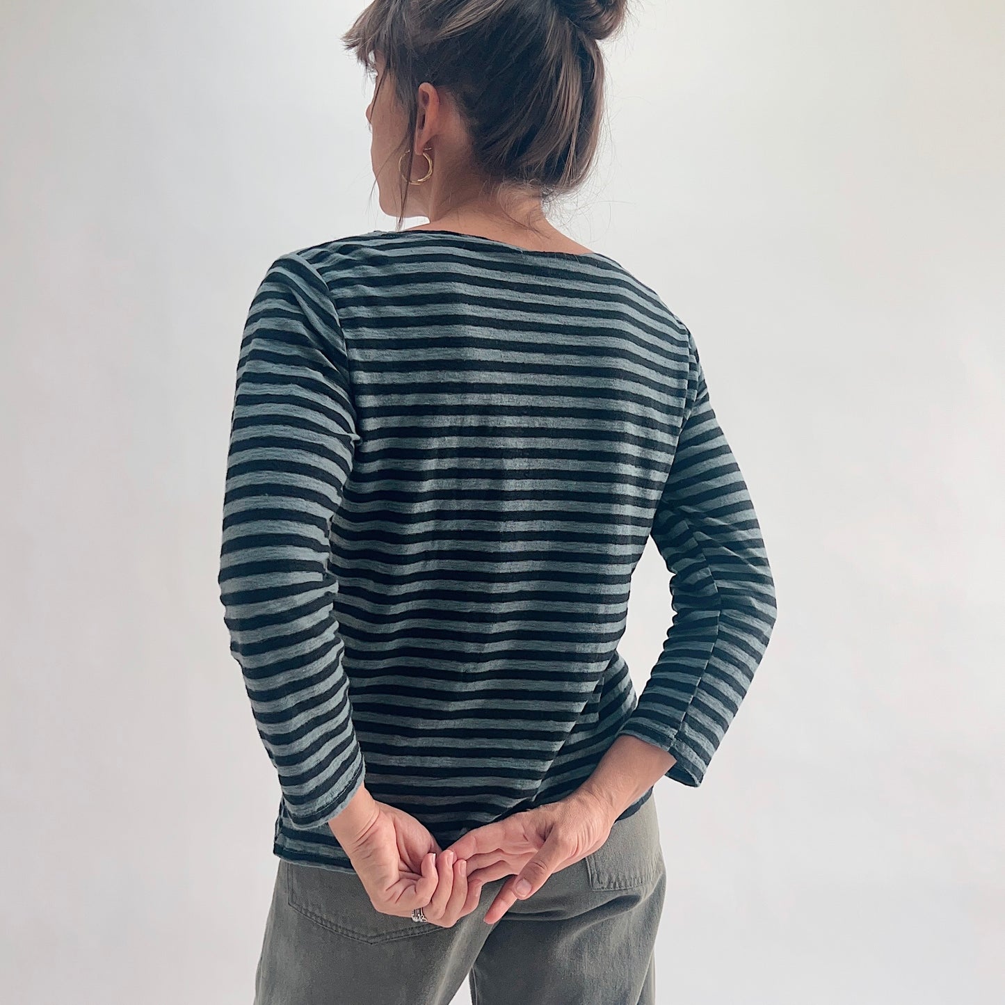 Back view of model wearing an iron stripe 3/4 sleeve boatneck tee, hands clasped behind her back, showing the clean back seam and 3/4 sleeve length.