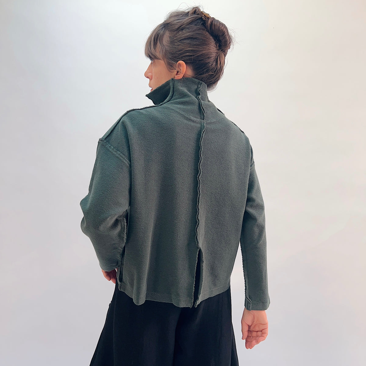 Eleven Stitch Funnel Jacket in Konbu, back view showing the center back seam with raw-edge detail and high funnel collar in forest green cotton terry