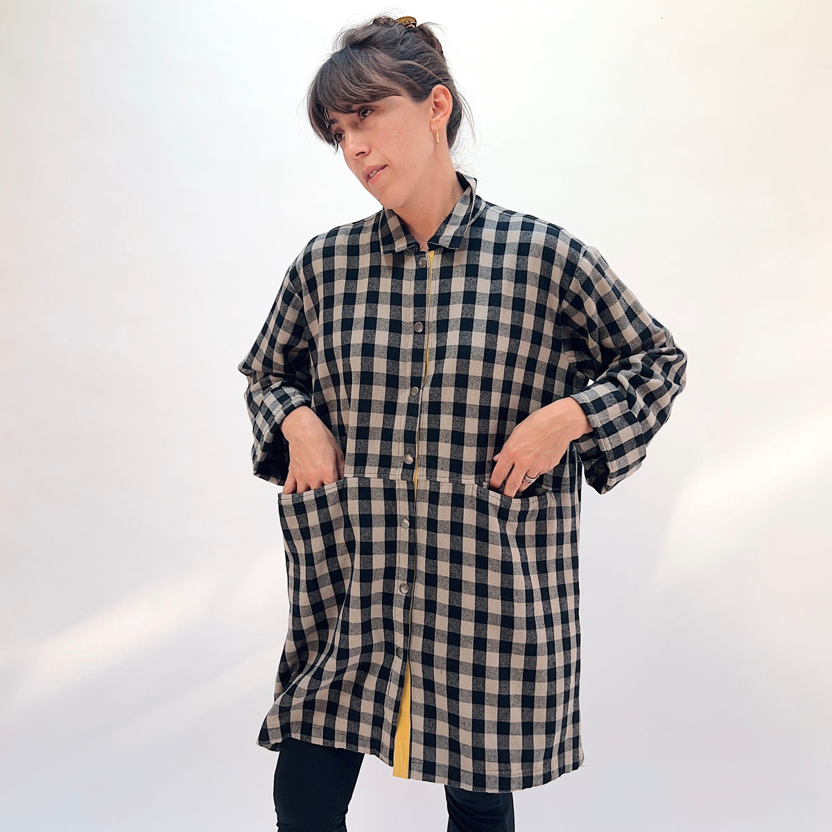 Eleven Stitch Duster in Fennel, front view with hands in pockets showing the two large hip patch pockets, mustard contrast placket, and snap side vents in black and natural gingham check flannel