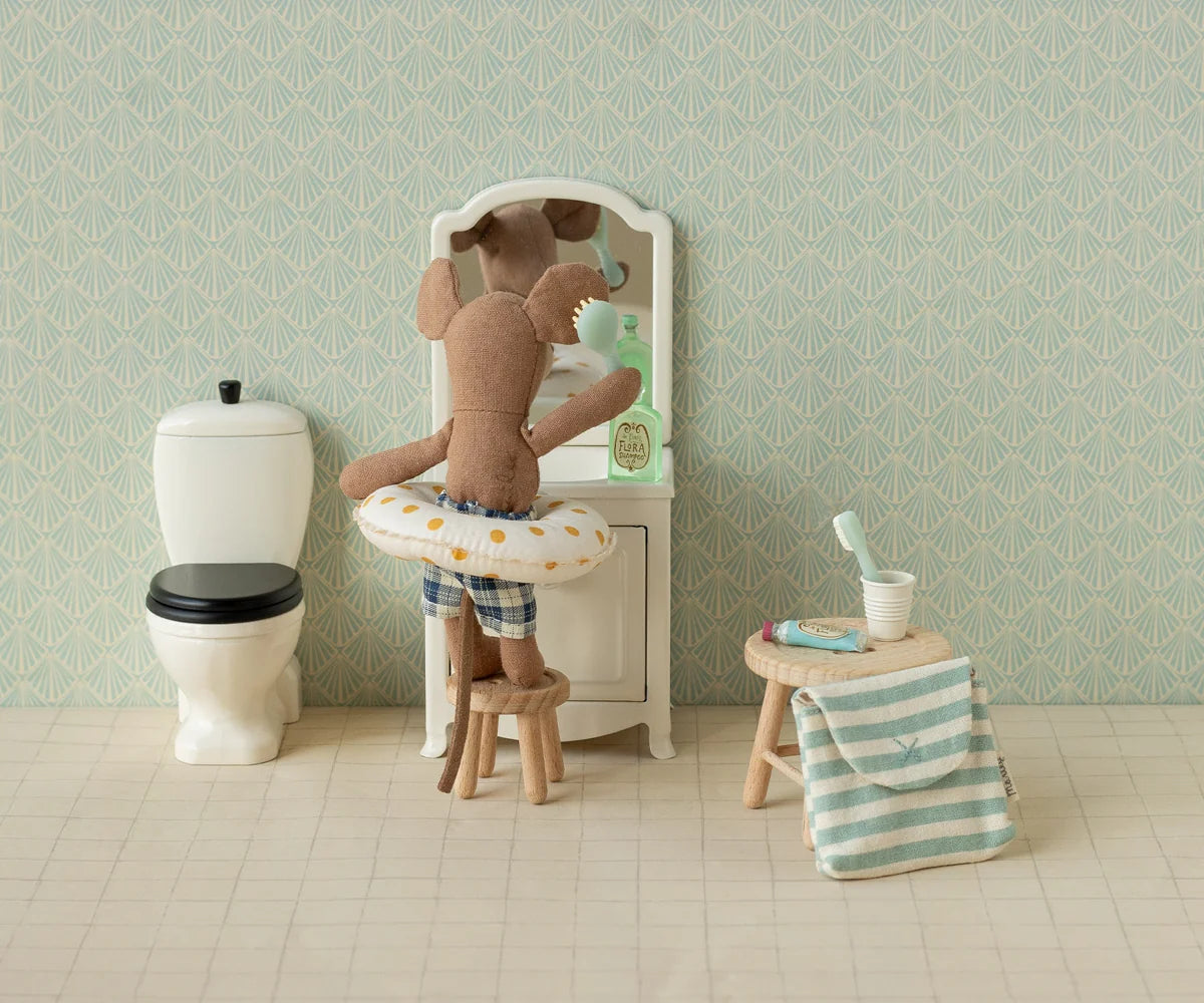 Maileg Toothbrush Set in Blue Striped Bag — lifestyle scene of a Maileg mouse doll in plaid swim trunks brushing teeth at a miniature vanity mirror, with the blue striped bag and toothbrush accessories displayed on a wooden stool nearby