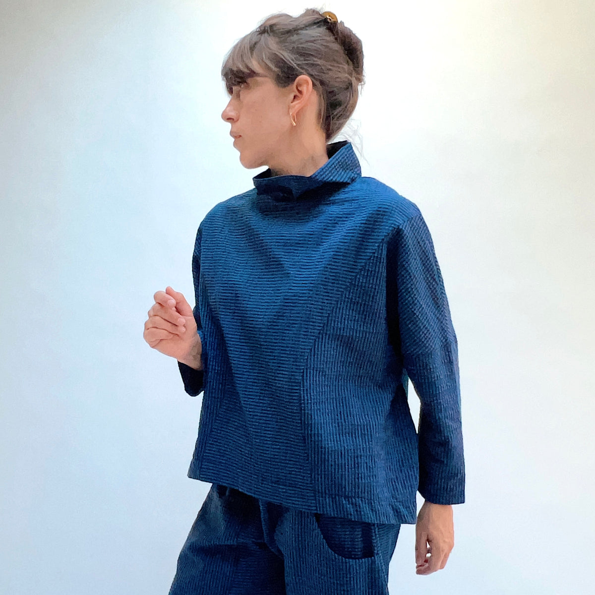 Niche Sofi Top in Blue Seersucker Stripe, three-quarter front view showing the cropped hip length and high funnel neck in teal and black seersucker stripe