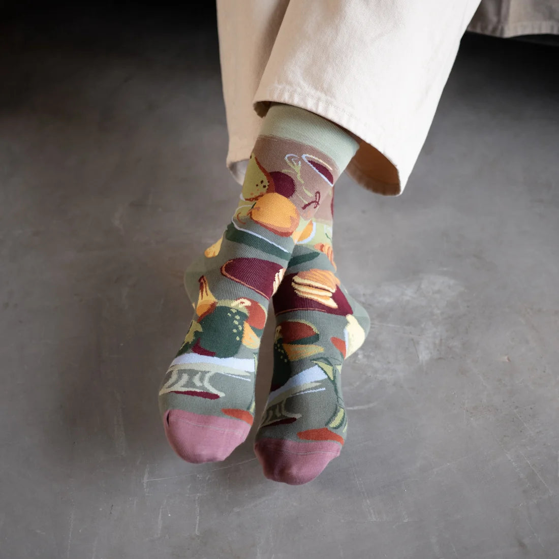 Bonne Maison Le Brunch Socks styled on feet showing the crew length and all-over brunch illustration in olive, burgundy, and terracotta