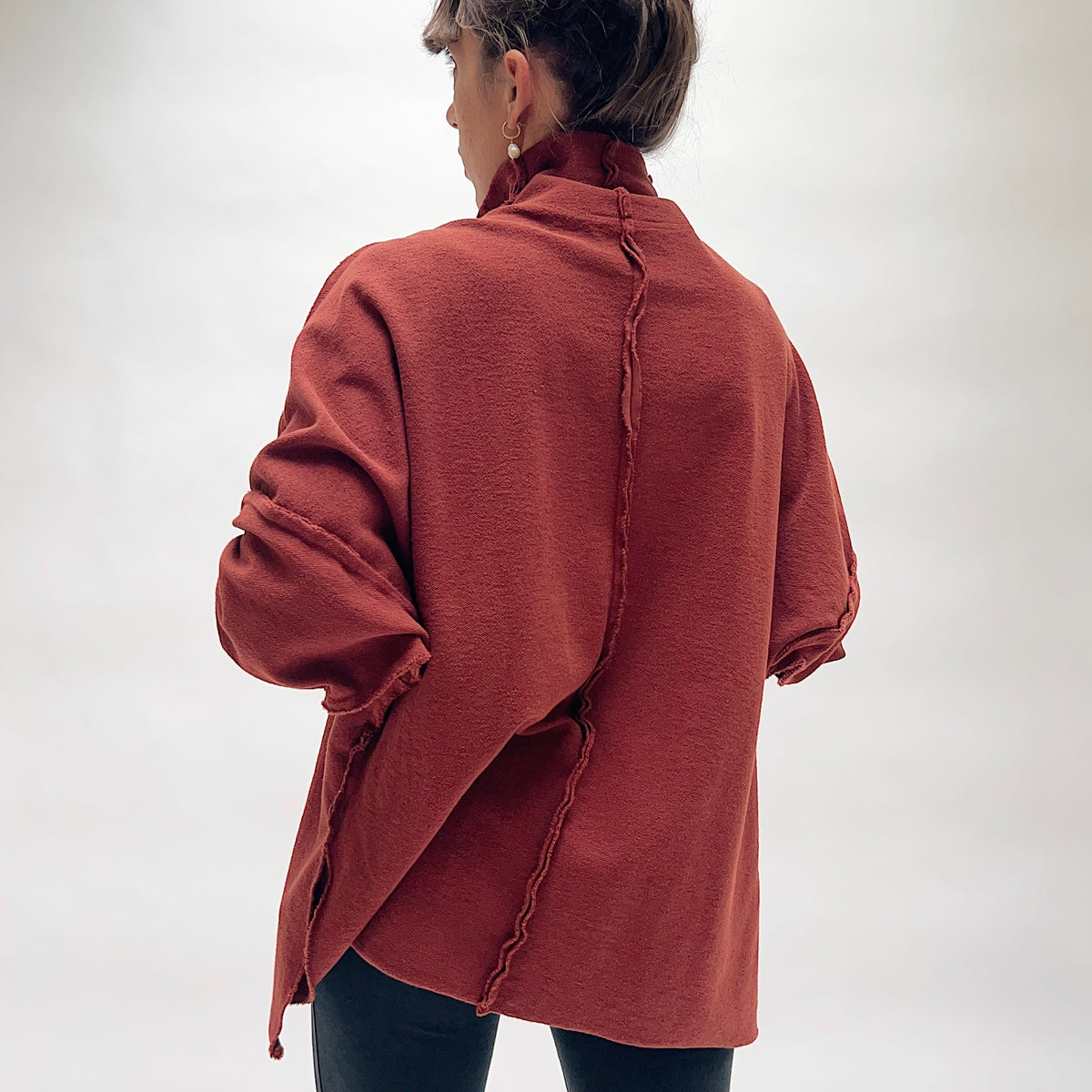 Back view of the Eleven Stitch Long Funnel Neck Slub Sweatshirt in Ginger Spice, showing the exposed raw center back seam, drop shoulders with raw seam detailing, tunic length, and side slits in warm terracotta slub cotton