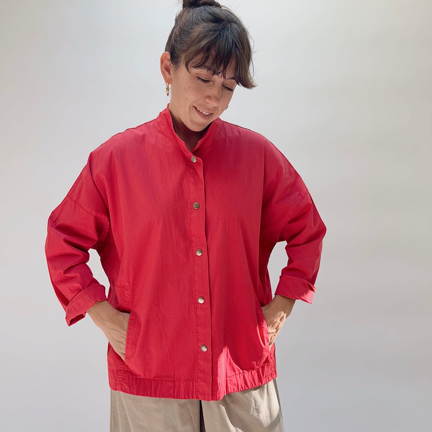 Eleven Stitch Stand Collar Jacket in Cayenne, full front view on model with hands in pockets, showing stand collar, metal snap closures, two front pockets, and elasticated hem detail, paired with khaki wide-leg trousers