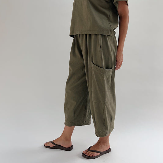 Side view of model wearing Bryn Walker jasper Pasha pant, showing large patch pocket detail, wide-leg drape, and banded hem at ankle