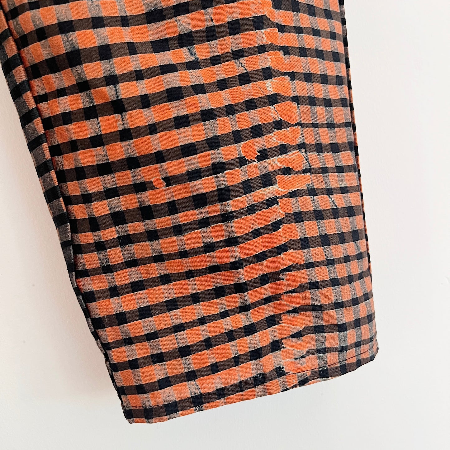 Close-up of hand-dyed persimmon orange and black batik grid fabric on Lazy Pants in Persimmon Grid, showing the handcrafted print texture