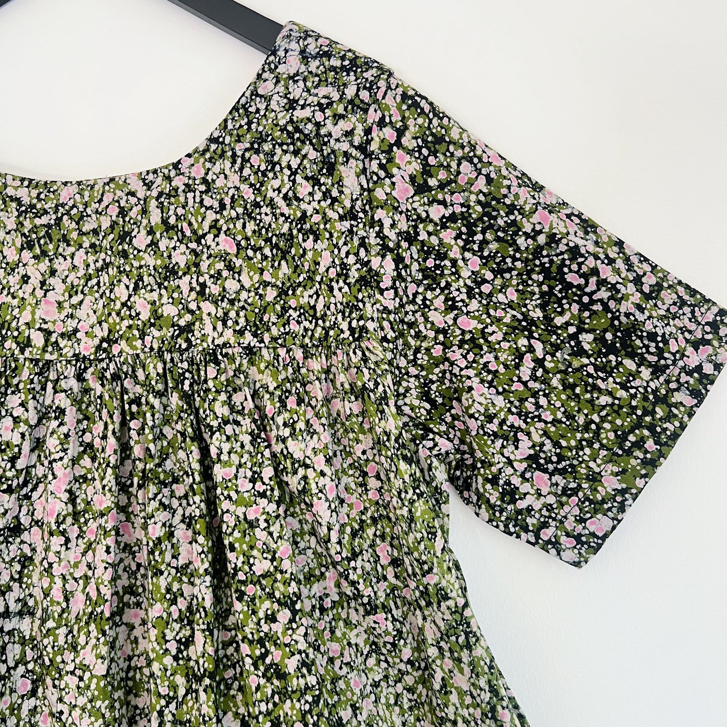 Close-up of the upper bodice and sleeve of the Sakina Dress in Green and Pink Speckle, highlighting the round neckline, gathered yoke seam, short sleeve hem, and hand-printed green, pink, and white speckle pattern on dark navy Batiki cotton with natural dye variation