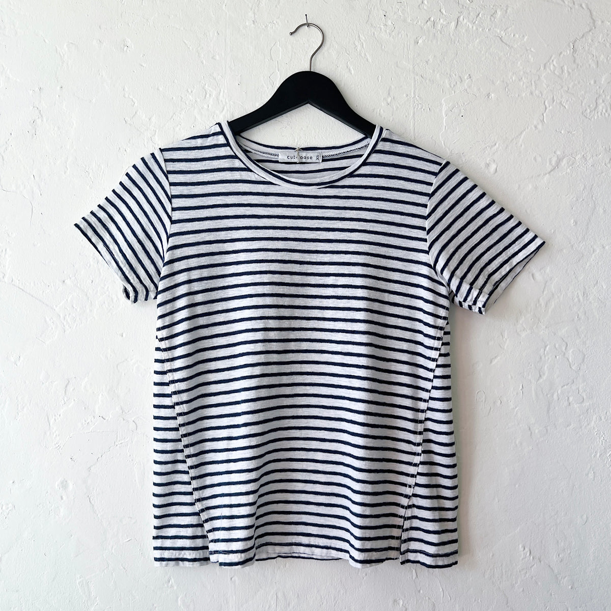 A striped navy and white short sleeve tee with slit hem, displayed on a hanger against a white wall.