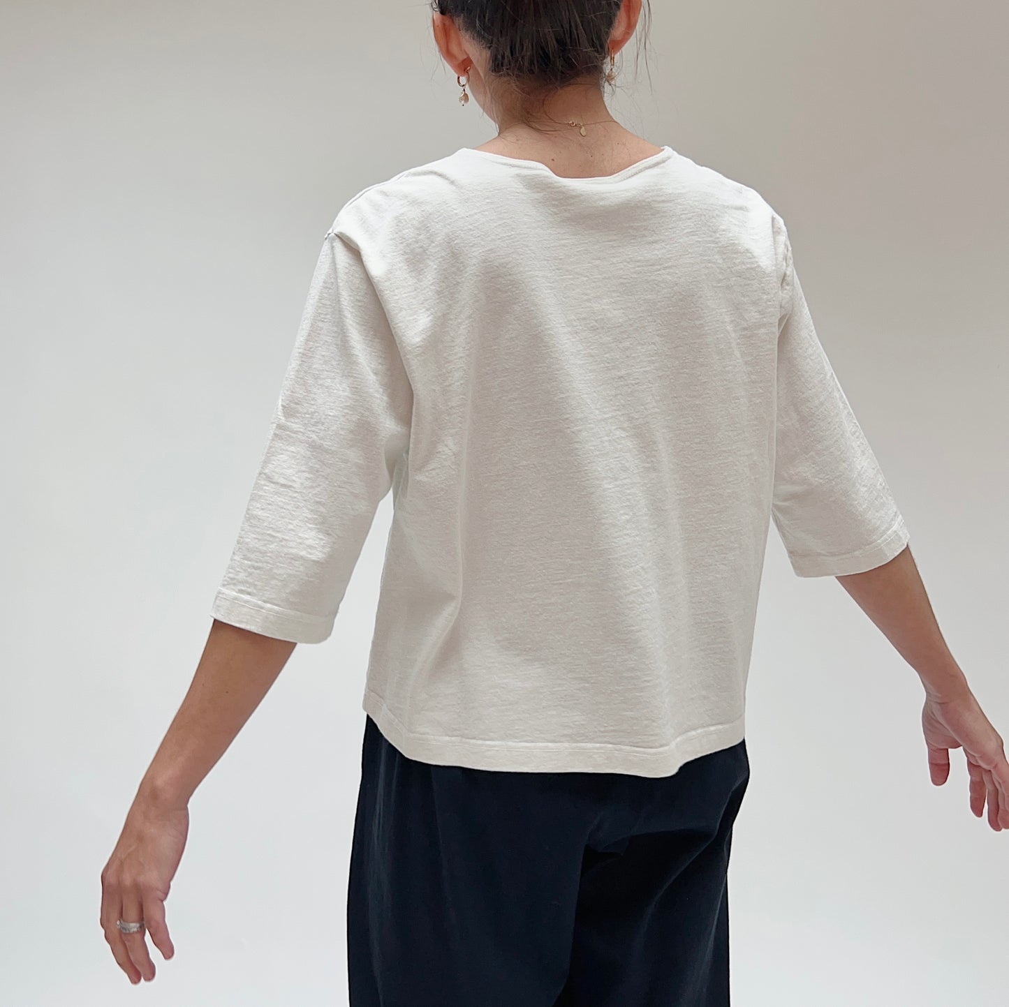 A person wearing a white, 3/4 sleeve cotton top with two front pockets, made by Pacific Cotton.