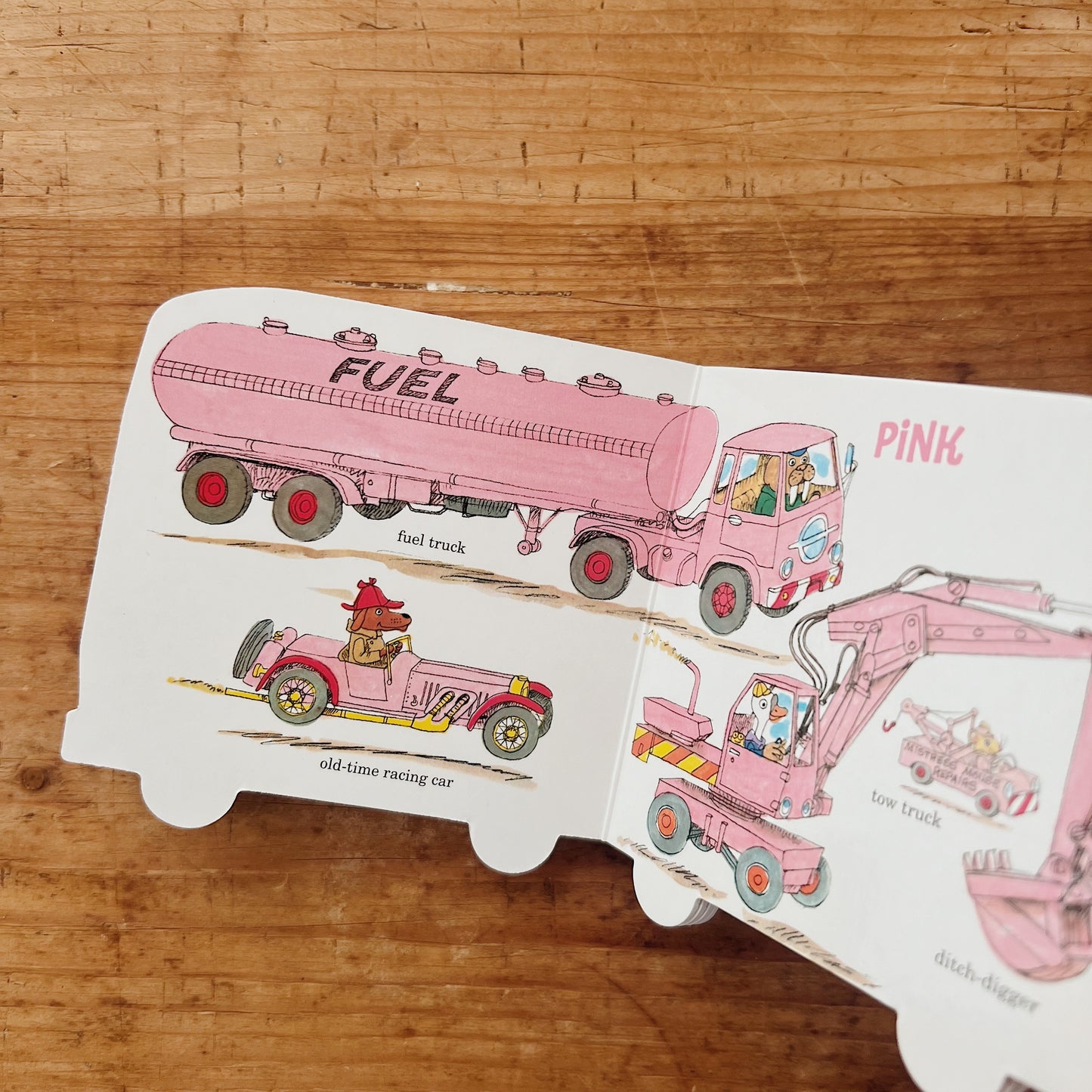 Interior spread of Richard Scarry's Colorful Cars and Trucks showing illustrated pink vehicles labeled fuel truck, old-time racing car, tow truck, and ditch digger, under the heading PINK