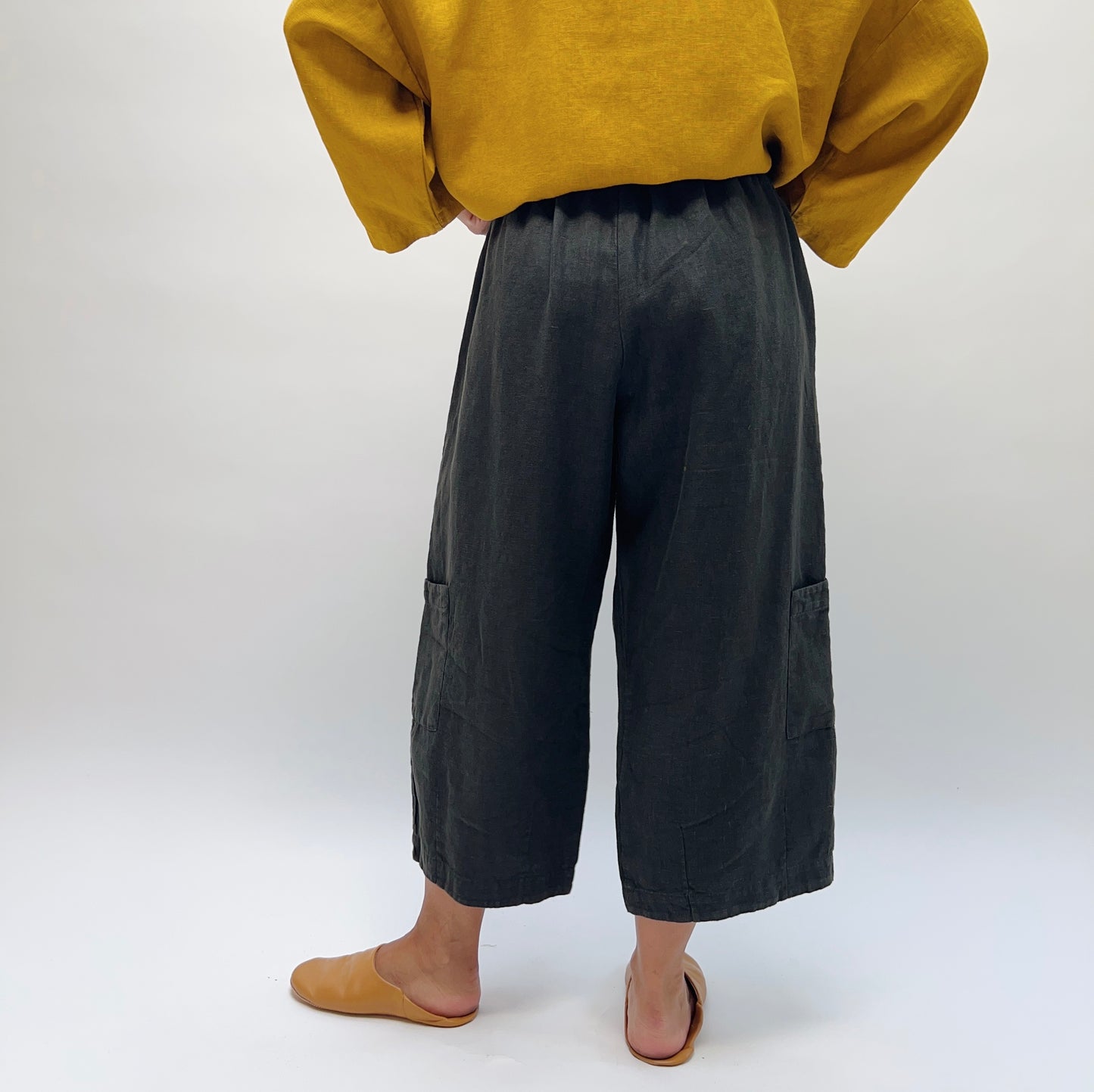 Back view of Bryn Walker Heavy Linen Casbah Pant in black, showing elastic waistband and two large patch pockets at the hem, styled with a mustard linen top