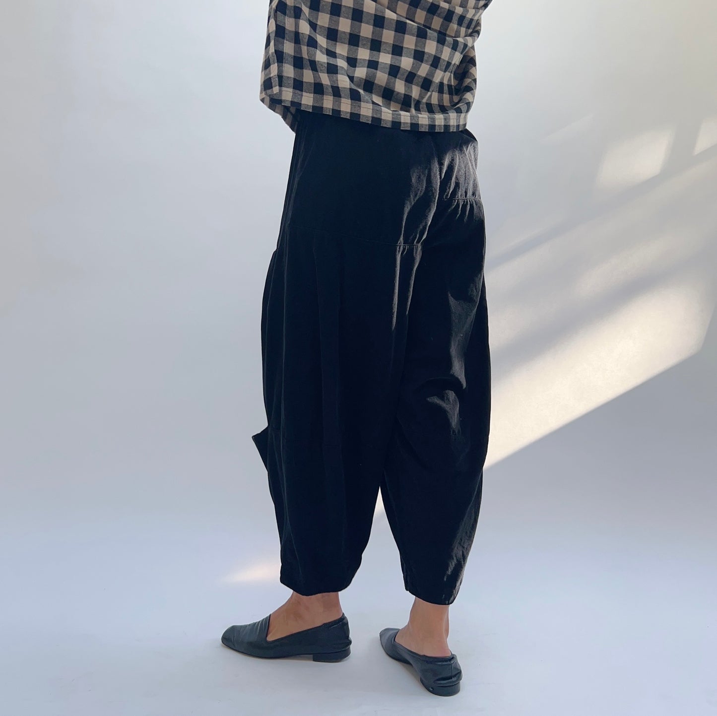 Side view of black corduroy pant showing elasticated waistband, voluminous drape, and tapered ankle with side pocket
