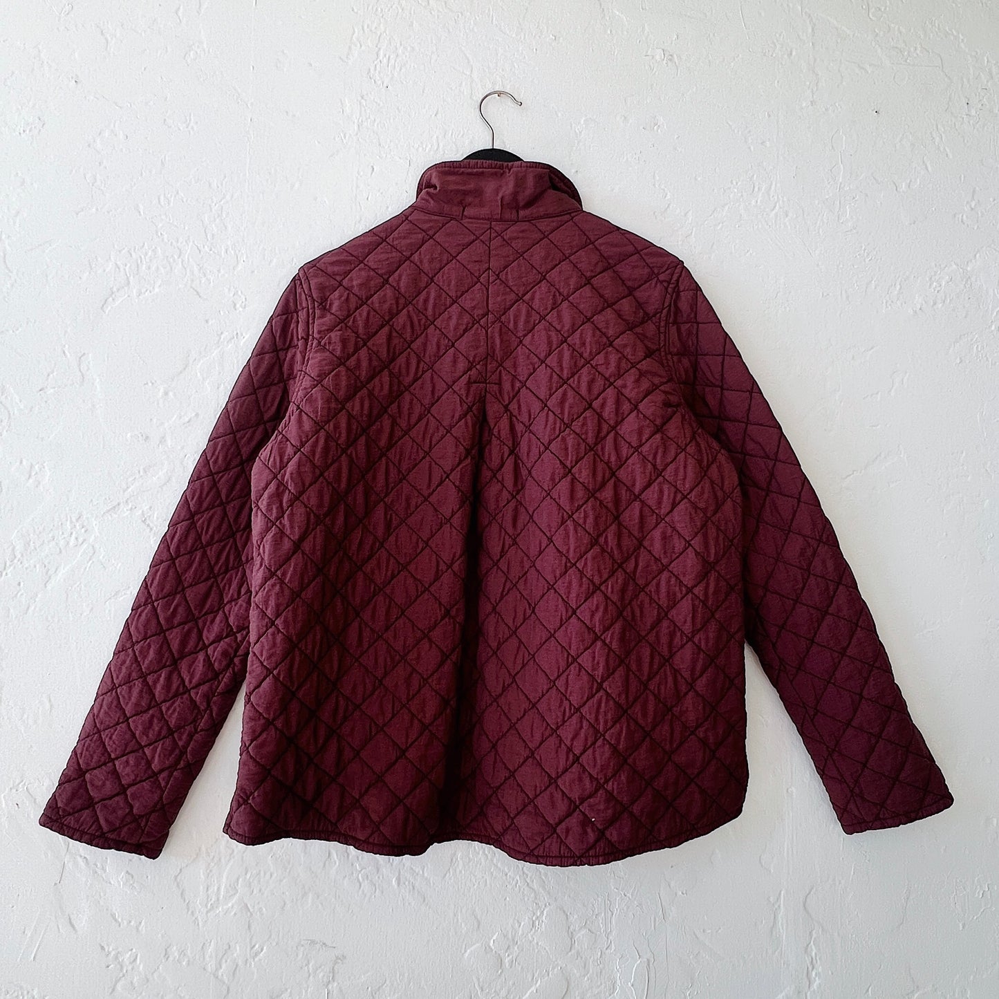 Quilted jacket on a hanger against a white wall, viewed from the back