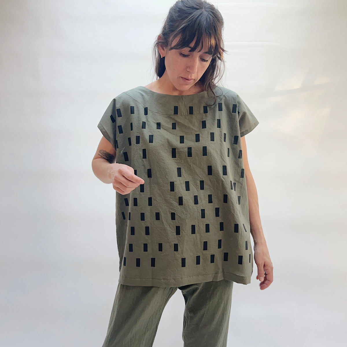 Model wearing the Uzi Disko Tunic in Army Green, full-length front view, loose army green 100% cotton tunic with allover hand screen-printed black rectangle pattern and capped sleeves, styled with matching army green pants