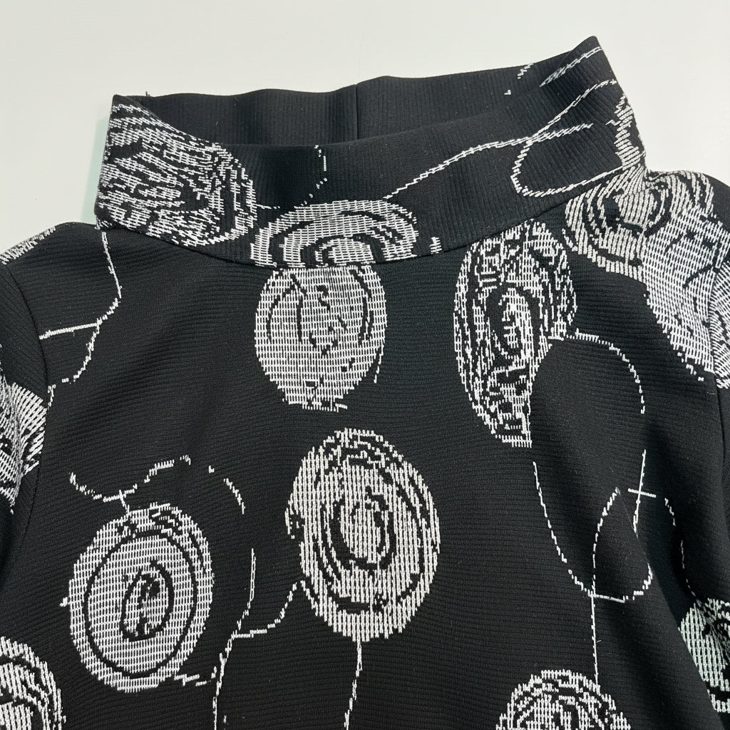 Close-up of Christopher Calvin Knit Mock Neck Top in Circle Print showing folded mock neck collar detail and white crosshatch-textured concentric circle woven jacquard pattern on black polyester-cotton knit
