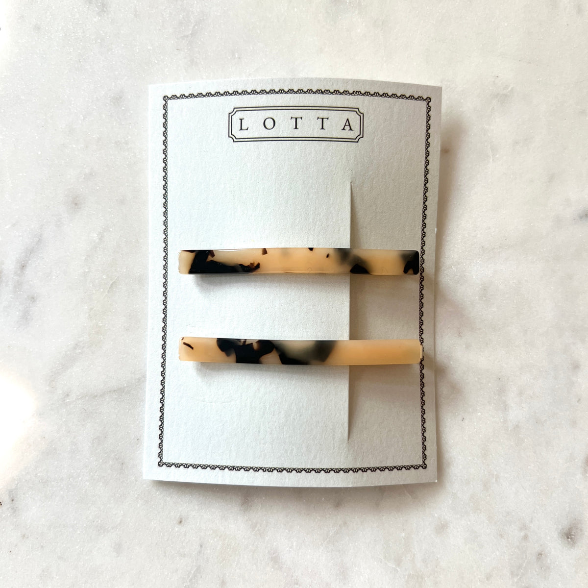 Two tortoiseshell hair clips on a white card with 'Lotta' branding on a marble surface.