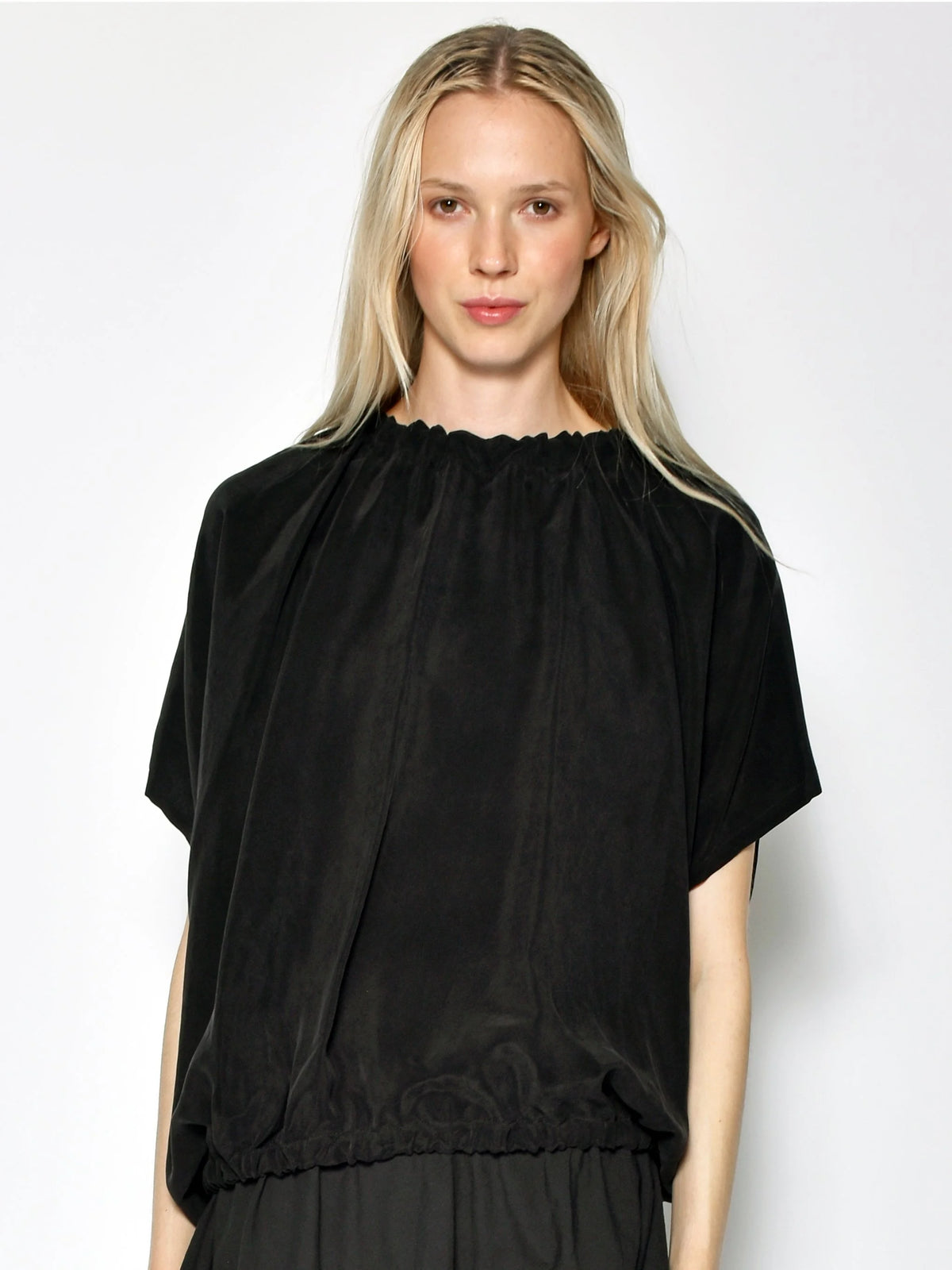 Front view of Uzi Cupro Nina Top in Black on a model, showing the gathered neckline, cap sleeves, and draped fabric.