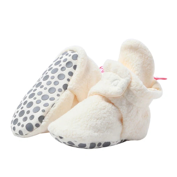 Cream fleece baby booties, with one tilted to show the dotted gripper sole included in sizes 12M and 18M.