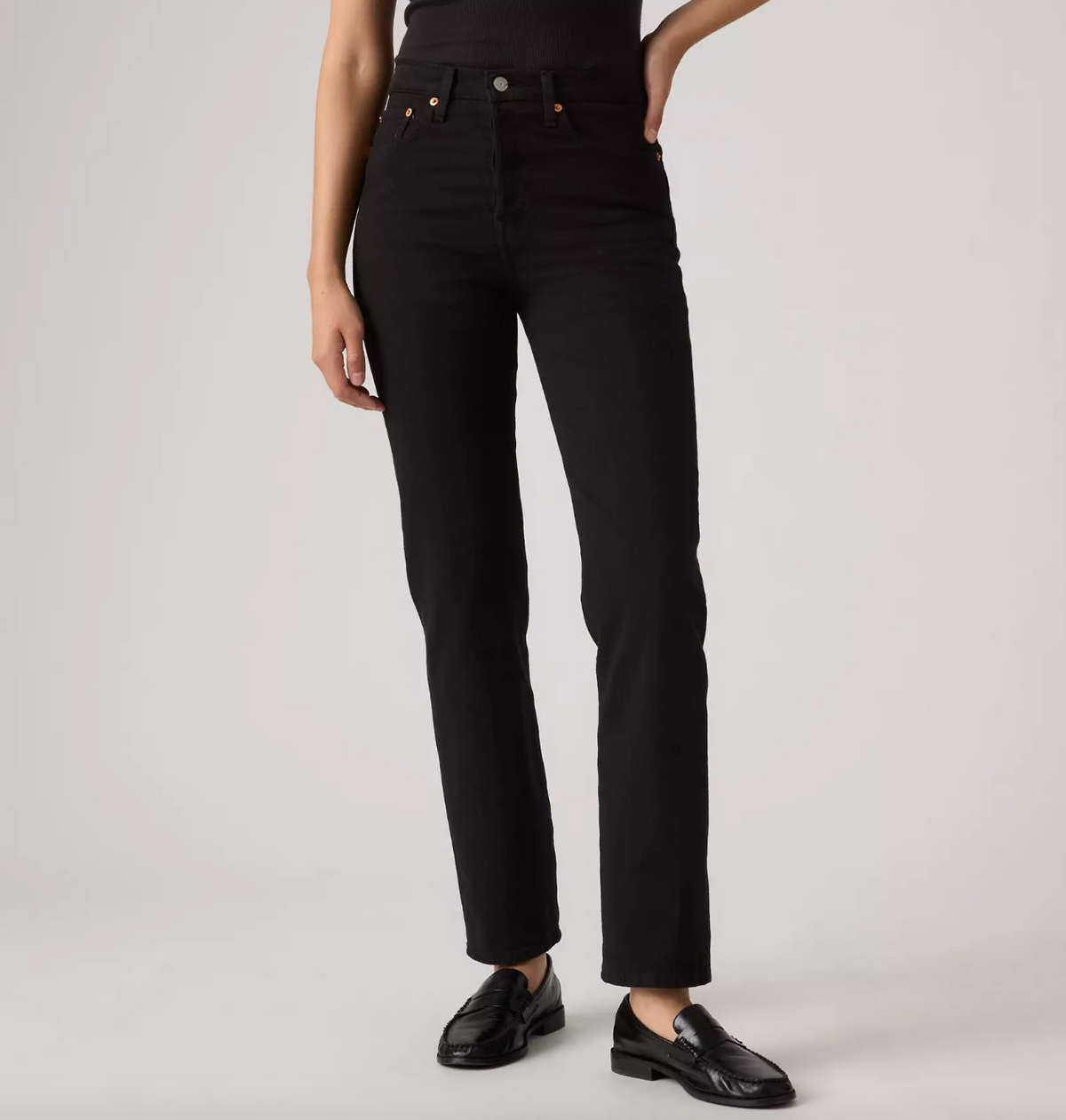 A model wearing black high-waisted straight-leg jeans and black leather loafers, shown from the waist down against a light gray studio background.