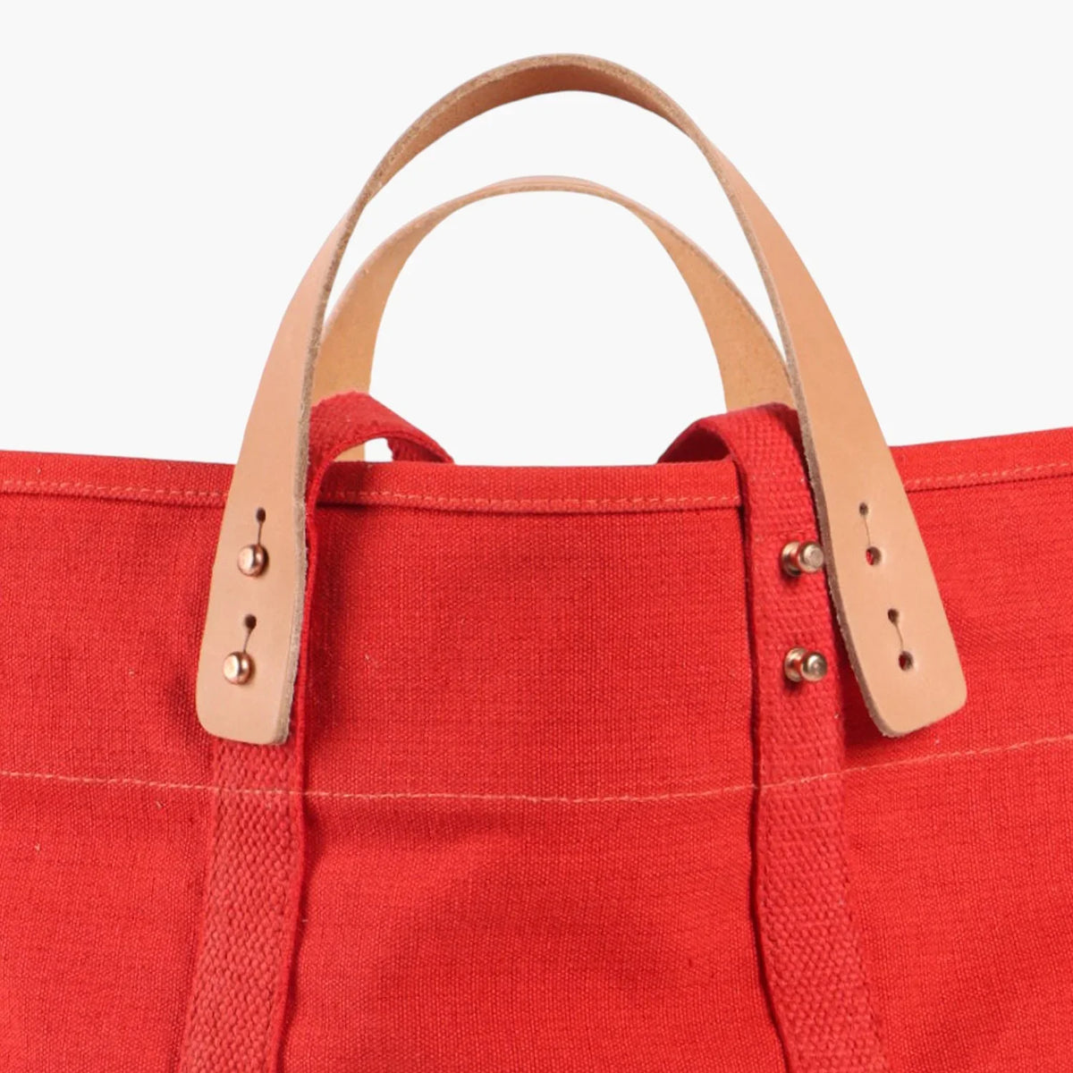 Close-up of the Persimmon tote's detachable natural leather handles, metal buttons, and webbing straps.