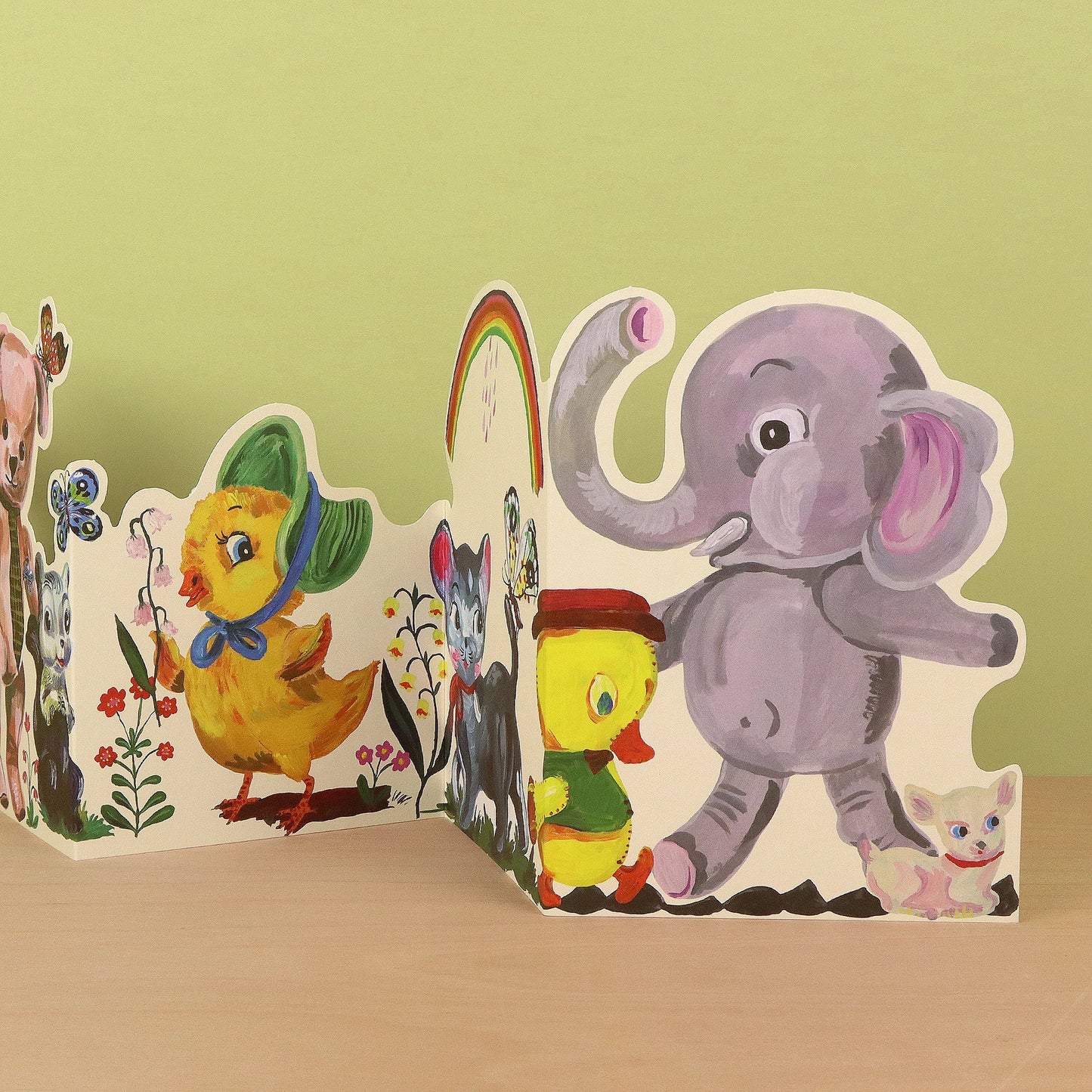 Close-up detail of the Plushie Party die-cut concertina card showing a yellow duck in a green hat, a small chick, a grey elephant, and a white kitten in a colourful vintage-style illustration by Nathalie Lété