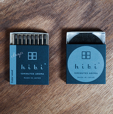 Two Hibi Cedar Wood Incense Match boxes in teal and navy on a wood surface — one open showing 8 match-style incense sticks, one closed with the Hibi 10 Minutes Aroma logo, Made in Japan