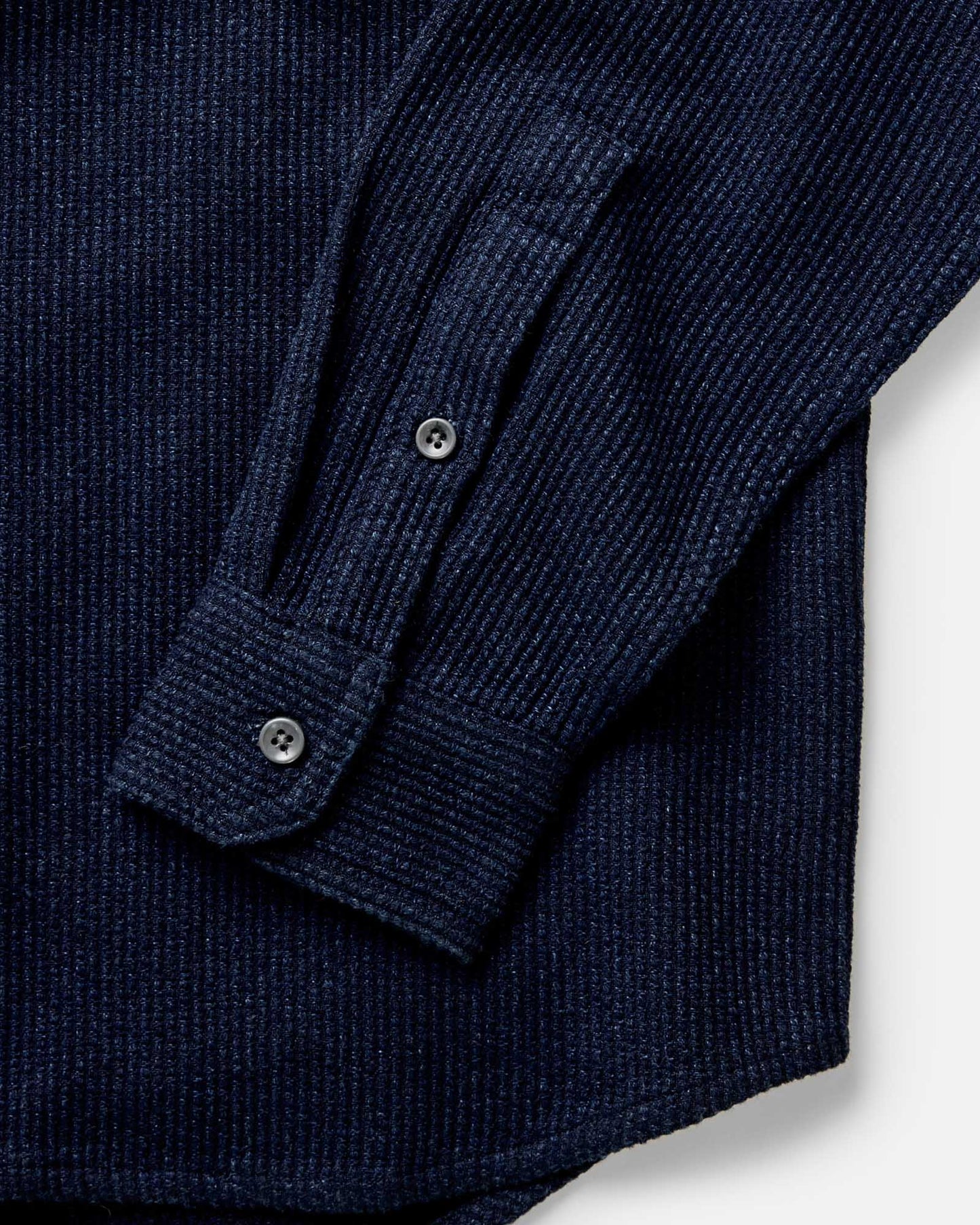 Close-up of Taylor Stitch Utility Shirt in Rinsed Indigo Sashiko showing buttoned cuff and sleeve detail with dark corozo-style buttons and pronounced horizontal sashiko weave texture on deep rinsed indigo organic cotton