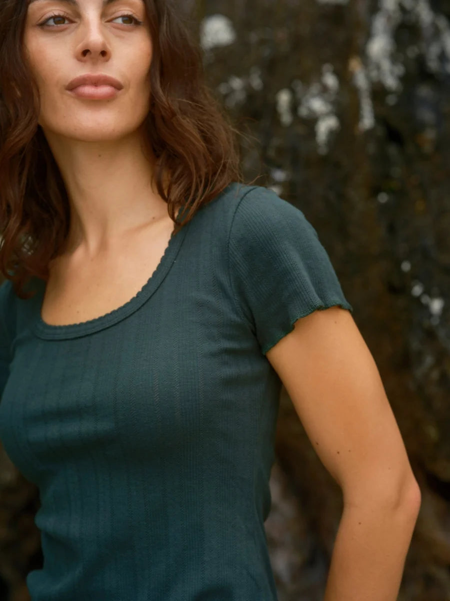 Close-up of female model wearing the Mollusk Surf Shop Pointelle Tee in Black Forest, showing scoop neck ruffled trim, short sleeve detail, and deep teal pointelle rib fabric texture