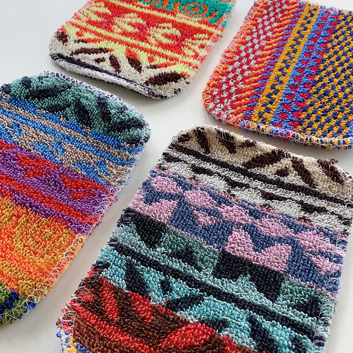 Close-up diagonal view of four colorful scrubby pads showing the detail of their woven cotton fibers.
