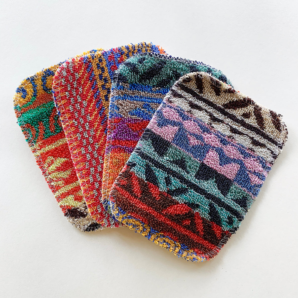 Flat lay view of colorful patterned scrubby pads fanned out in an overlapping stack on a white background.
