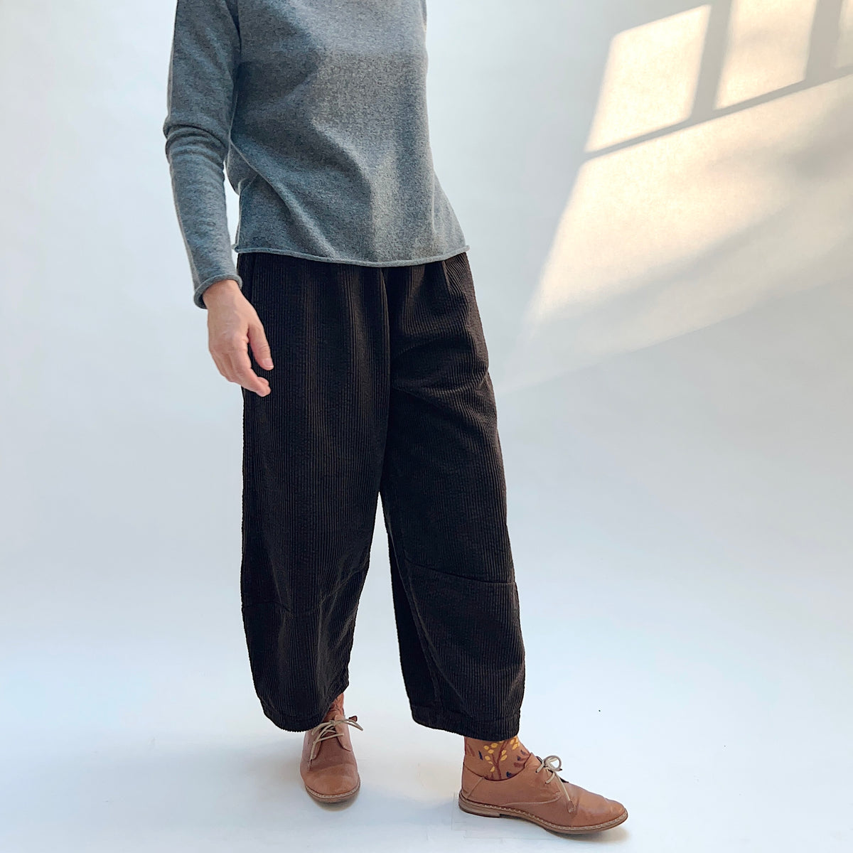 Angled front view of Lux Corduroy Lantern Pant in Chocolate on a model, showing the vertical corduroy ribs and curved lower-leg seams.
