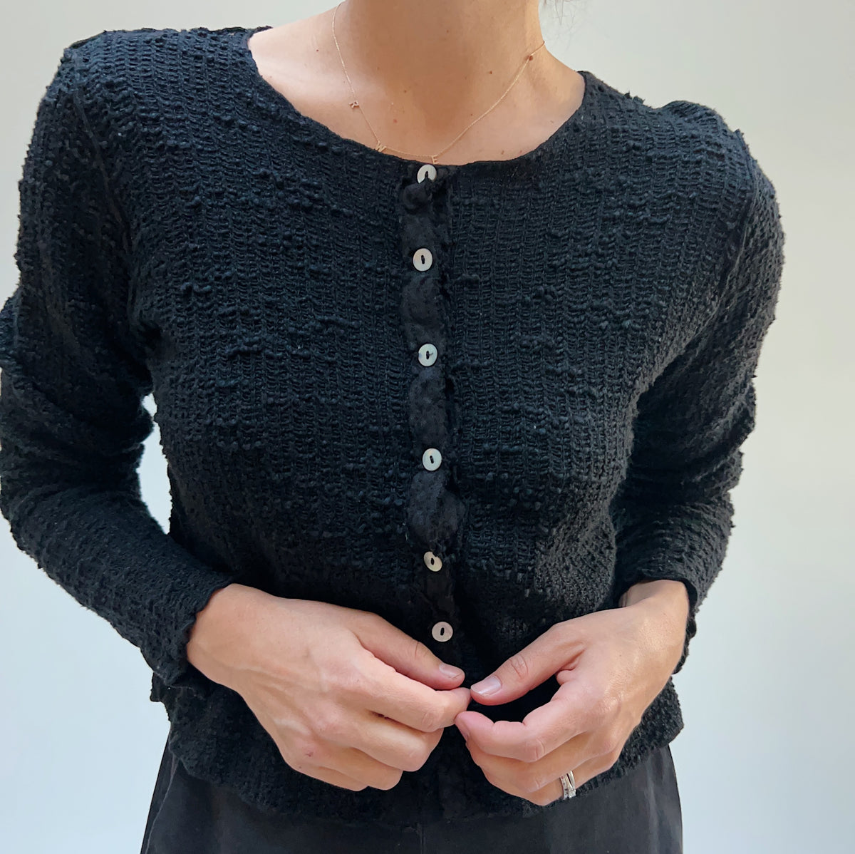 Close-up front view on a model of a black textured knit crop cardigan showing the fabric texture and button placket.
