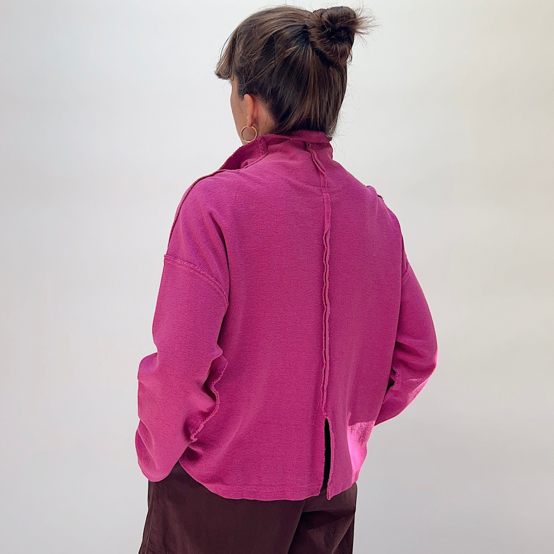 Eleven Stitch Funnel Jacket in Berry, back view on model, showing center back seam with frayed detail and back hem vent, paired with dark brown wide-leg trousers
