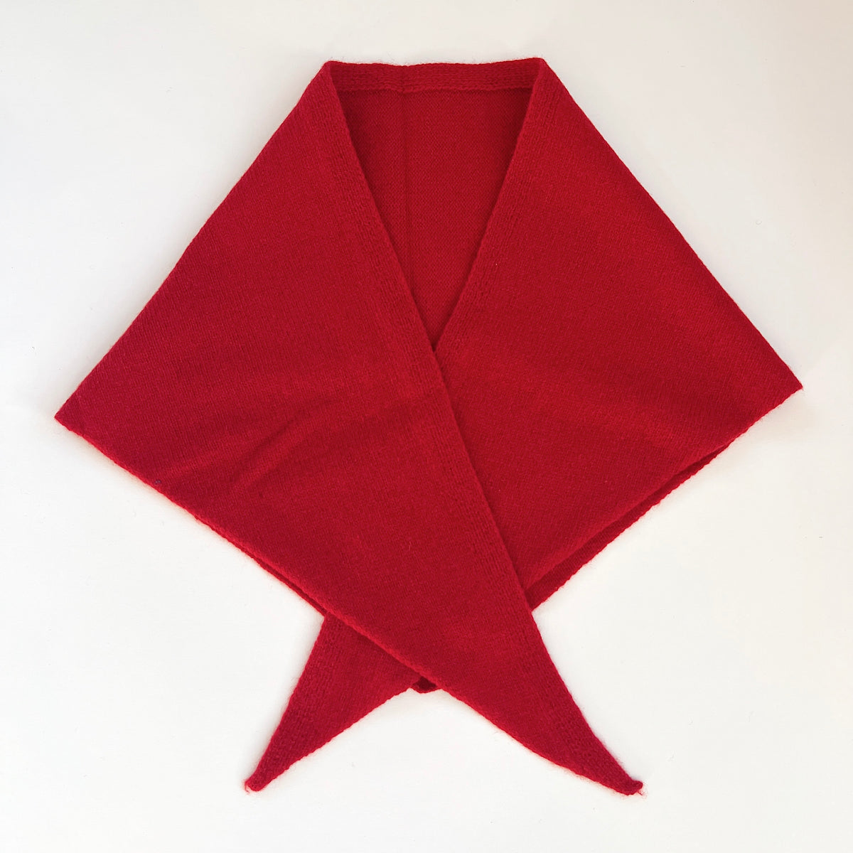 Flat lay view of the red merino wool triangle scarf with its long ends crossed in front.
