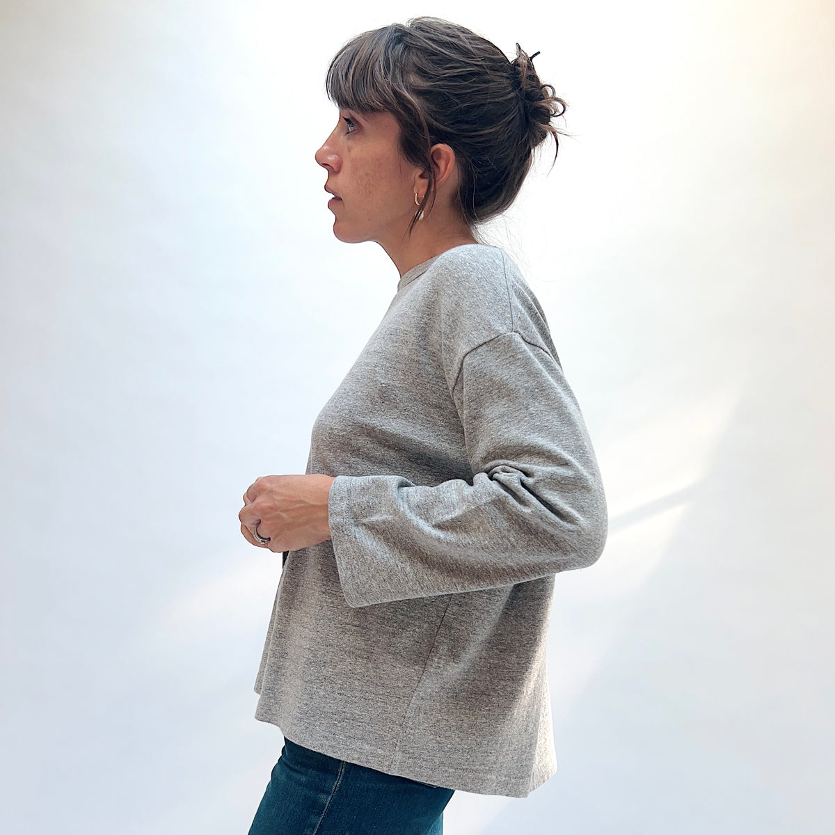 Side view of a model wearing the grey cotton knit pullover, showing the sleeves and straight hem.

