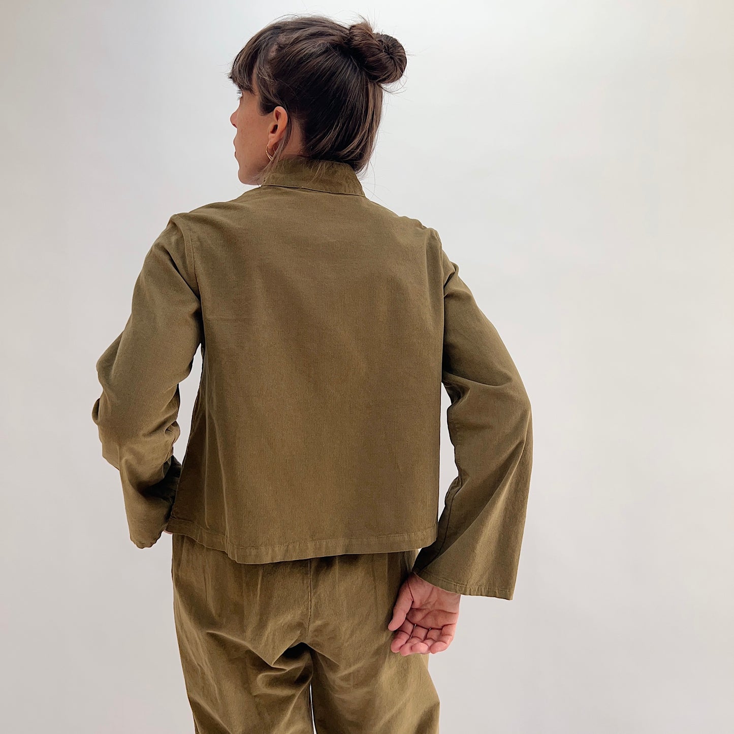 Back view of the Bryn Walker Corduroy Standing Collar Crop Jacket in Partridge, showing cropped hemline, wide sleeves, ruffled standing collar, and olive pinwheel corduroy texture, styled with matching Pasha Pants
