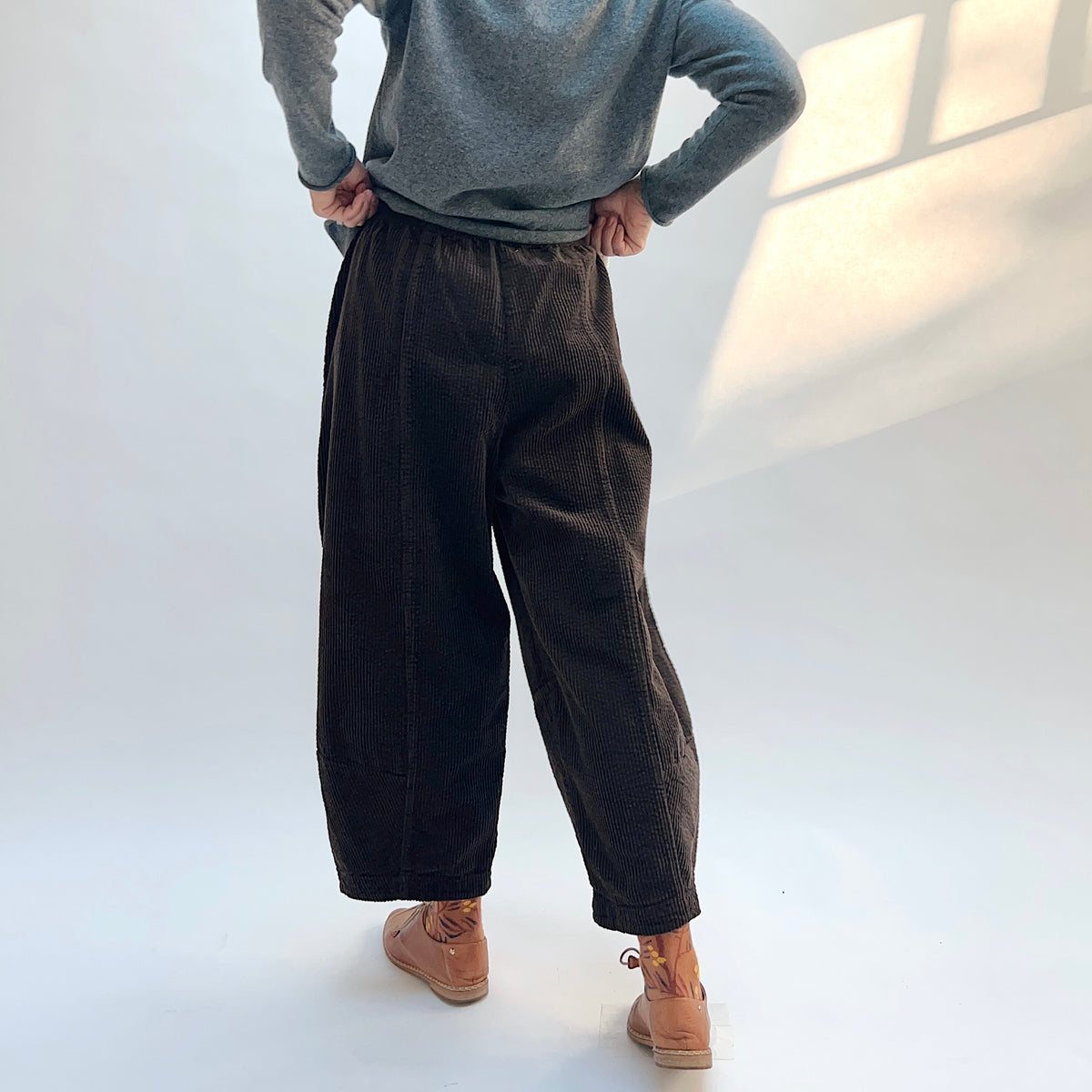 Back view of Lux Corduroy Lantern Pant in Chocolate on a model, showing the gathered waist and wide legs tapering toward the hems.
