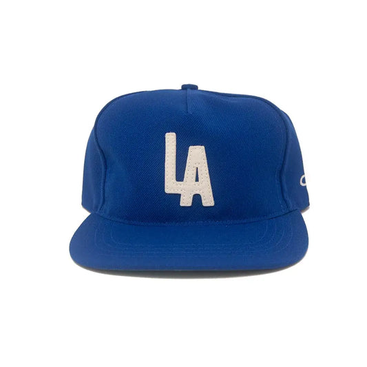 A royal blue baseball cap featuring a white embroidered 'LA' logo on the front, set against a plain white background.