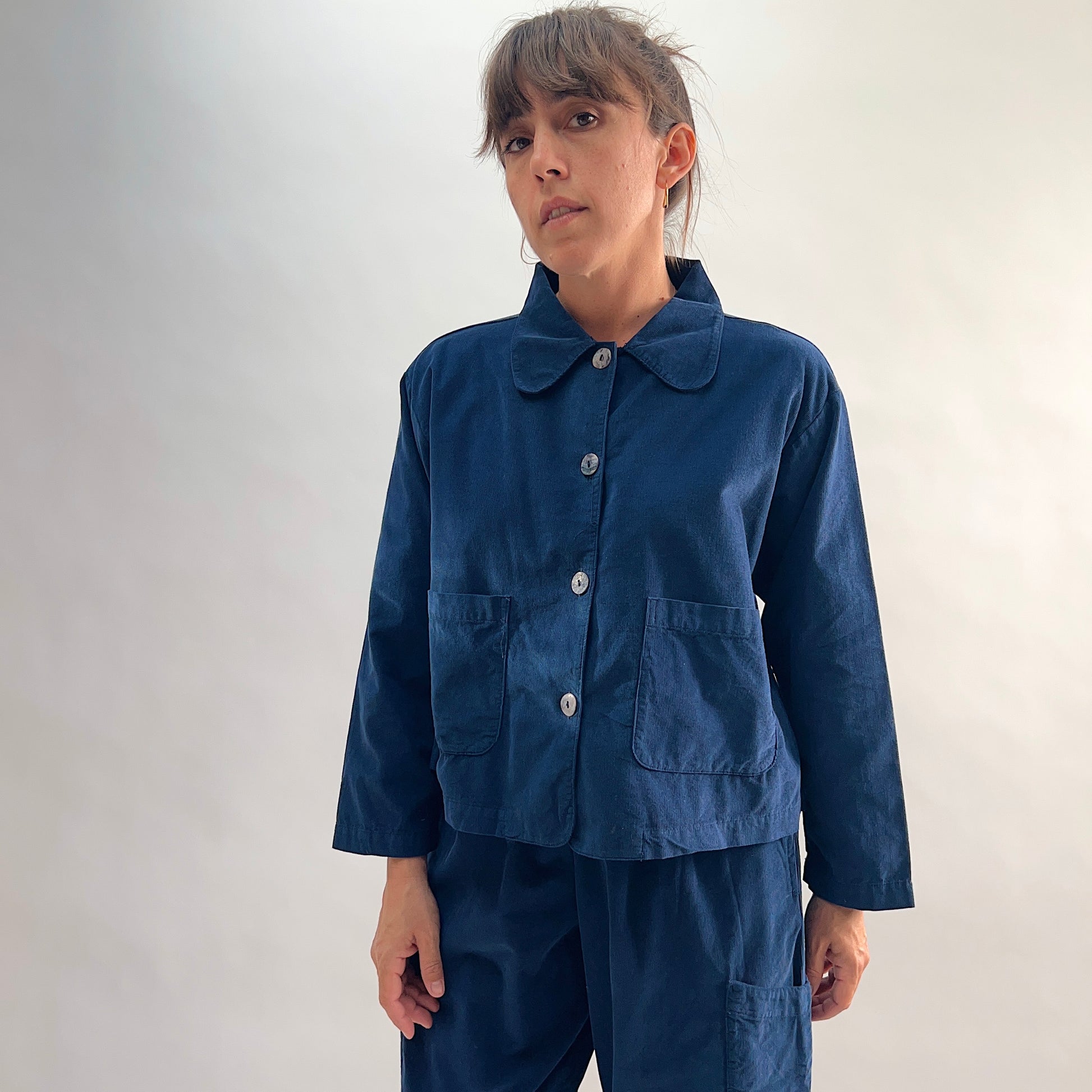 Model wearing the Bryn Walker Corduroy Audrey Jacket in Nova, front view showing rounded peter-pan collar, shell button closure, and patch pockets, paired with matching navy trous
