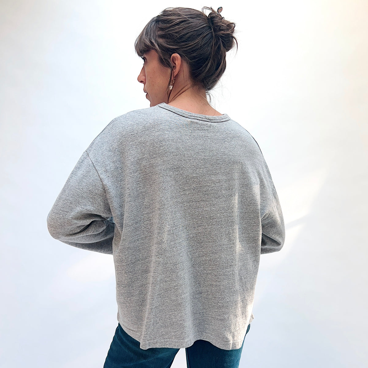 Back view of a model wearing the grey cotton knit pullover, showing the plain back and dropped shoulders.
