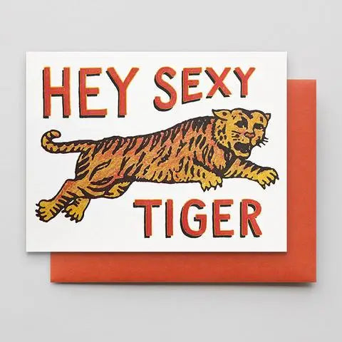 A square greeting card with a white front featuring the words “HEY SEXY TIGER” in red-orange lettering and an illustrated tiger in orange, yellow, and black, shown with a matching orange-red envelope behind it on a light gray background.