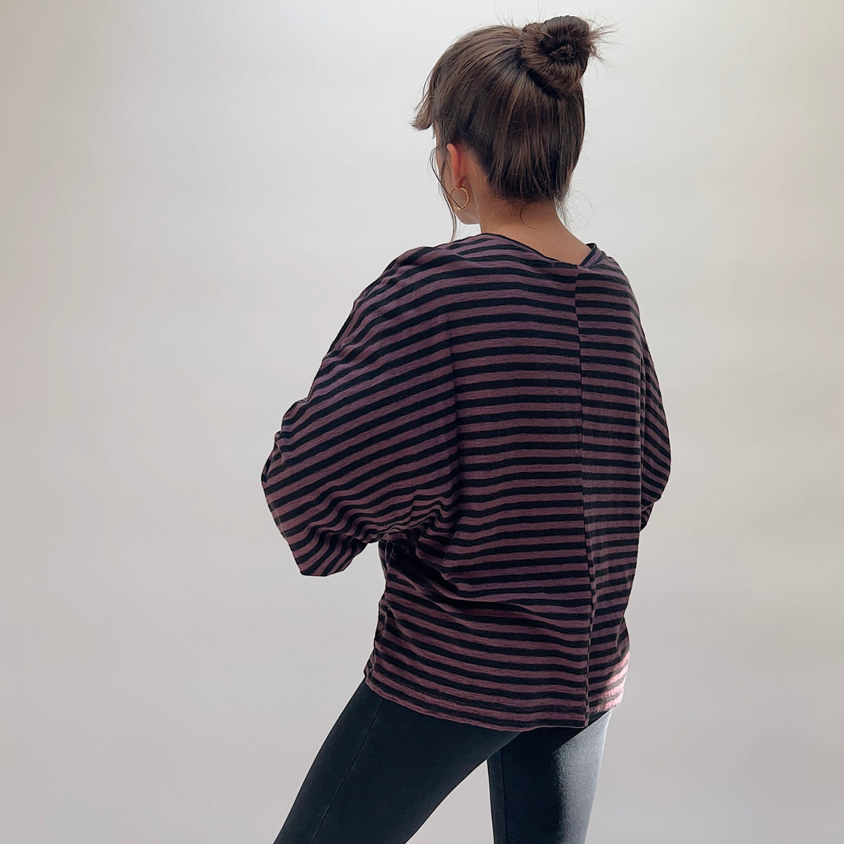 Back view of the Cut Loose Slouchy Raglan Tee in Cinnabark Stripes, showing the oversized drop-shoulder raglan silhouette, wide sleeves, and horizontal cinnabark and black stripe in a relaxed cotton-linen blend, paired with dark jeans
