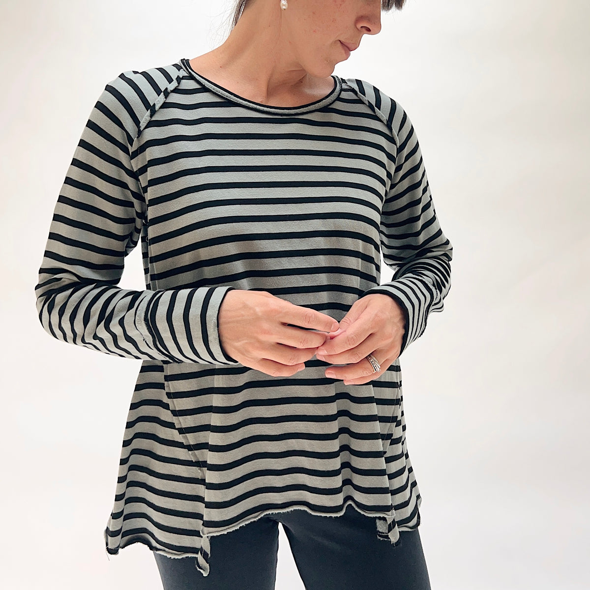 Model wearing the Cut Loose Striped Gore Tee in Seal from the front, showing the crew neckline, raglan sleeves, angled gore panels at the hem creating an A-line swing, and raw lettuce-edge hem in seal grey and black horizontal stripe, with thumb-hole cuffs visible at the wrists
