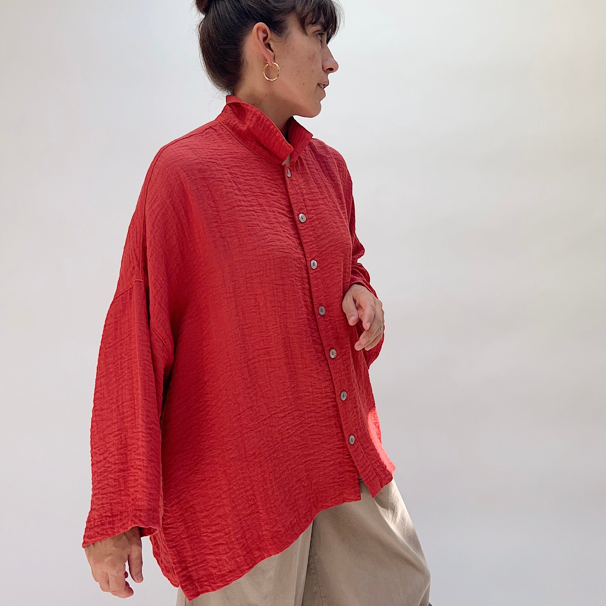 Eleven Stitch Travel Big Shirt in Pimento, side view on model, showing relaxed oversized silhouette, textured fabric, wood buttons, and curved hem with side slit, paired with khaki wide-leg trousers
