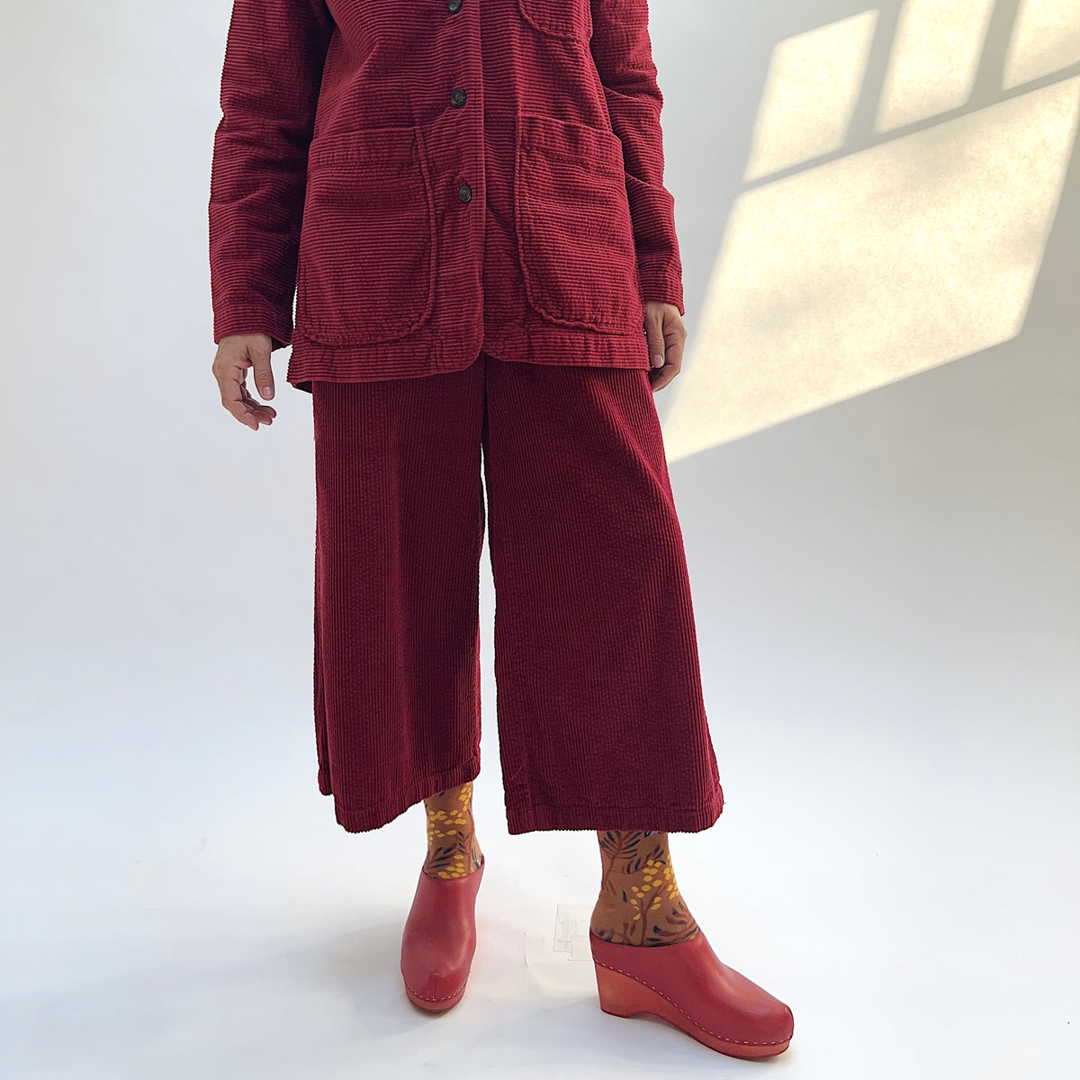 Model wearing the Cut Loose Lux Corduroy Crop Wide Leg Pant in Maraschino with a matching blazer, showing the cropped hems.

